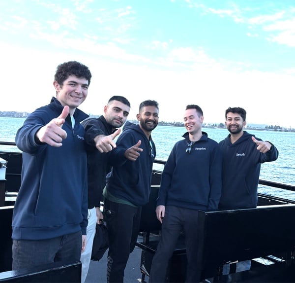 Five teammates in Senpilot shirts smiling beside the water