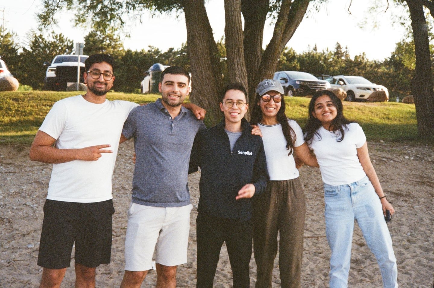Five teammates posing together under a tree